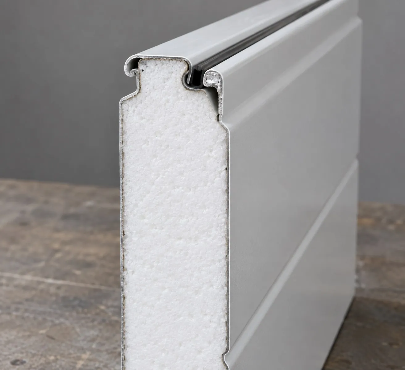 Cut end of an insulated steel garage door section showing the foam core between steel skins